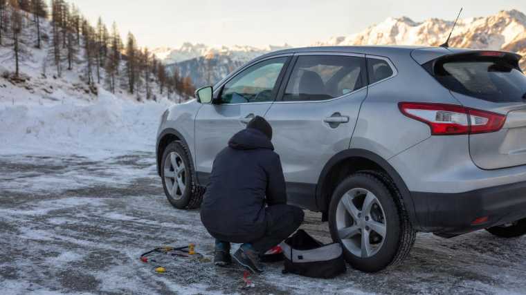 Handen die sneeuwkettingen naast een huurauto op een besneeuwde parkeerplaats klaarleggen