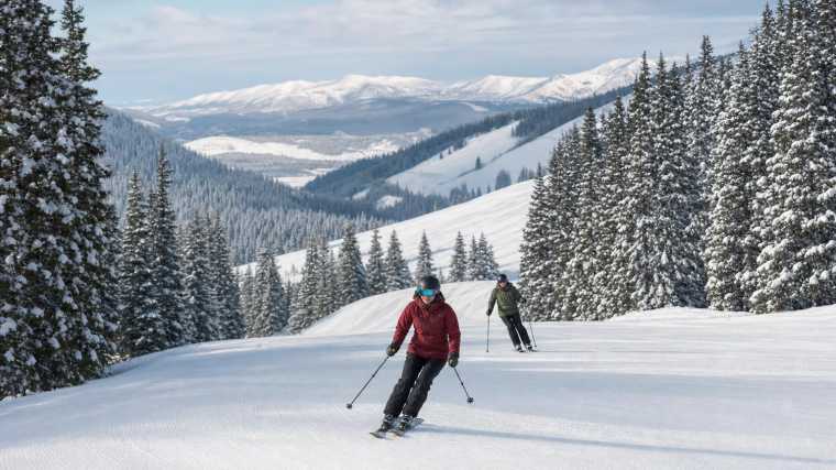 Een winters bergdal met skiërs op pistes tussen besneeuwde sparren en berghellingen