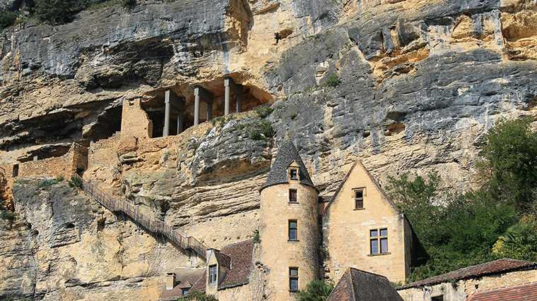 Een landhuis tegen de rotswand in La Roque-Gageac en de overblijfselen van het fort.