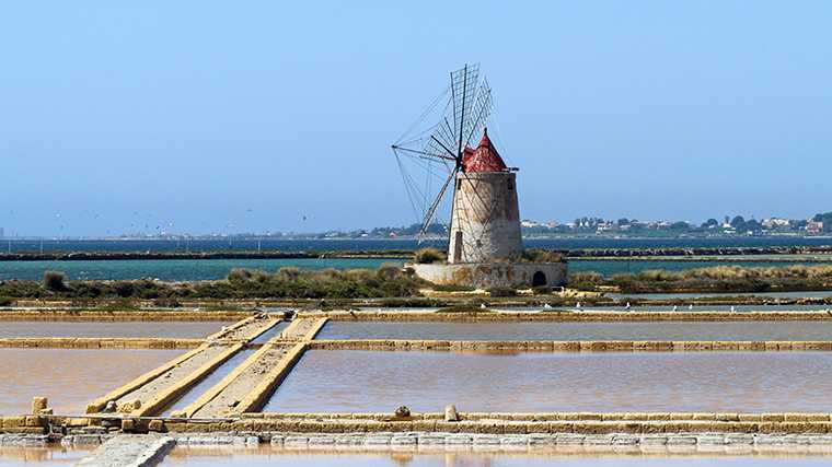 Een traditionele windmolen midden tussen de zoutpannen bij Trapani in het westen van Sicilië.