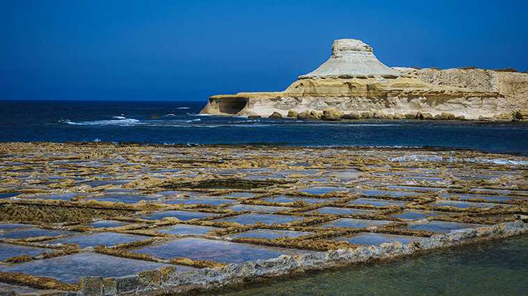 De zoutpannen en de kegelvormige rots bij de baai Xwejni op Gozo.