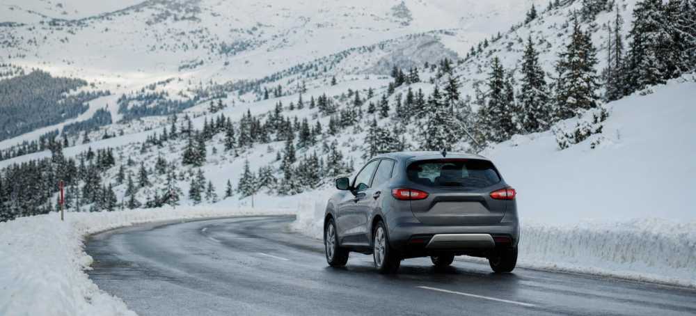 Huurauto op een besneeuwde bergweg met winterse bomen op de achtergrond