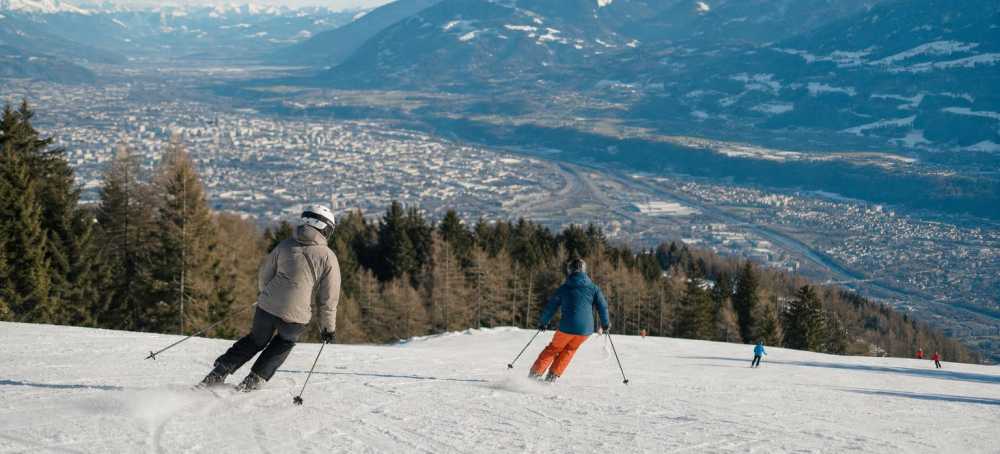 Skiërs op een brede piste met Innsbruck en de omliggende bergen in de verte